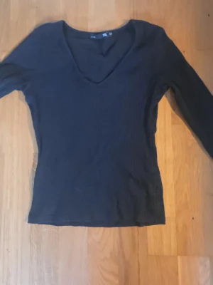 Svart ribbad långärmad topp lager 157 - En svart ribbad långärmad topp från 157 med v-ringning. Toppen är i stretchigt material och har en smickrande passform som passar perfekt till jeans eller kjol. Enkel och stilren design som funkar till många olika looks.