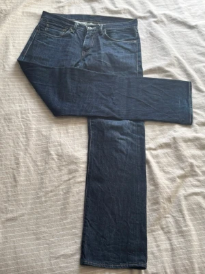 Mörkblå raka jeans från Levi's - Snygga mörkblå jeans från Levi's med klassisk rak passform och fem fickor. Jeansen har kontrastsömmar och en brun läderpatch bak i midjan. Tillverkade i slitstark denim med en tidlös look och diskret röd Levi's-tag på bakfickan.