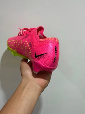  Mercurial rosa fotbollsskor - Säljer ett par  Mercurial fotbollsskor i en riktigt snygg rosa färg med gula detaljer och svart logga. Skorna har en låg profil, snörning och en neonfärgad sula med Zoom-teknologi för extra grepp och fart på planen. Priset kan diskuteras. Passar även , 45,5