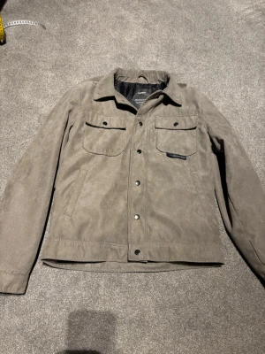 Beige mockaimitationsjacka med knappar - Snygg beige jacka i mockaimitation från Pull&Bear 🤎 Jackan har två bröstfickor med knappar, klassisk krage och tryckknappar framtill. Stilren och enkel design med en modern touch.  Säljs inte längre hos Pull&Bear! Perfekt jacka inför hösten och funkar även utmärkt under våren. 🍂  PRUTBART!