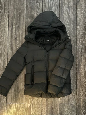 Svart J.Lindeberg vinterjacka - Säljer en svart pufferjacka från J.Lindeberg med huva och dragkedja framtill.  Jackan har två sidofickor med dragkedja och en quiltad design. Riktigt skönt material på insida, perfekt för kalla dagar och som sagt riktigt skön att bära. Passar dig som gillar en stilren och enkel vinterjacka. Nypris 2900kr 💰 men säljs inte längre vad jag vet. Den är i riktigt bra skick, ett pyttelitet hål synns på bild men inget märkvärdigt.