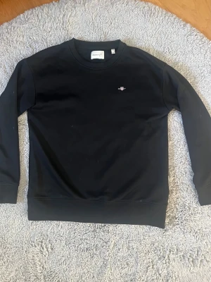 Svart Gant sweatshirt  - Säljer denna jättefina, Gant sweatshirt. Tröjan är från gant och är i jättebra skick. Inga hål eller slitningar. Är i storlek XS men passar också utmärkt som 170. Skriv bara vid funderingar. Försöker att posta samma dag som köpet!