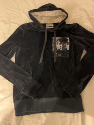 Limitato hoodie - Snygg svart hoodie i mjuk velour från Limitato med en unik patch med foto på bröstet. Huvan har kontrastfärgat foder och långa snören. Perfekt för dig som vill sticka ut med en exklusiv och konstnärlig look.
