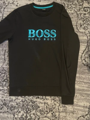 Svart sweatshirt från Hugo Boss - Svart sweatshirt från Hugo Boss med blått tryck på bröstet. Bra tröja nu in för hösten. Skriv vid mista fråga elle fundering. Priset är ej spikat. Storlek M