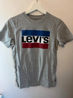 Grå Levi's t-shirt  - Snygg grå t-shirt från Levi's med klassisk stor logga i blått, vitt och rött framtill. T-shirten har rund halsringning och korta ärmar. Tillverkad i mjuk bomull som är skön att bära hela dagen.