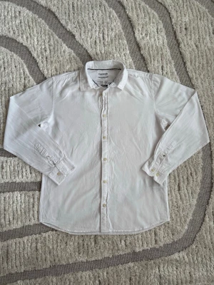 Vit klassisk skjorta från Essentials - Snygg vit skjorta från Essentials med klassisk krage och knäppning framtill. Tillverkad i mjuk bomull som känns skön mot huden. Perfekt till jeans eller chinos för en clean och enkel stil. Långa ärmar med knappar vid manschetterna.