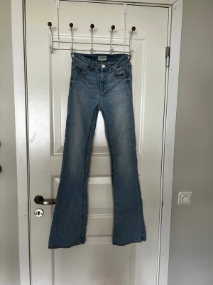 Ljusblå bootcut jeans från ONLY - Säljer ett par ljusblå bootcut jeans från ONLY i storlek XS. Jeansen har klassisk femficksmodell, hög midja och utsvängda ben. Tillverkade i mjuk denim med snygga slitningar och kontrastsömmar. Perfekta för en avslappnad och trendig look.