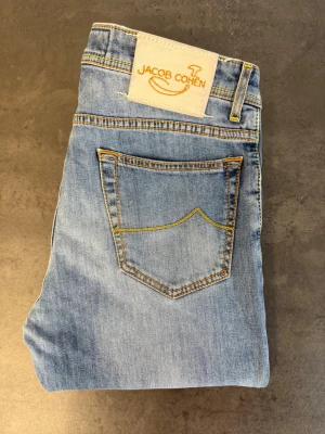 Ljusblå jeans från Jacob Cohen Type 688.C, Stl 33 - Snygga ljusblå jeans från Jacob Cohen med klassisk femficksmodell och kontrastsömmar. Jeansen har en rak passform och är tillverkade i mjukt denimtyg. Perfekta för en avslappnad och trendig look.
