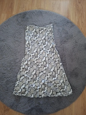Beige långkjol med ormmönster H&M - Beige långkjol från H&M med ormmönster i svart och vitt. Kjolen har en lätt utsvängd siluett och är gjord i ett mjukt, tunt material som känns skönt mot huden. Perfekt för dig som gillar trendiga prints och vill ha en statement piece i garderoben.