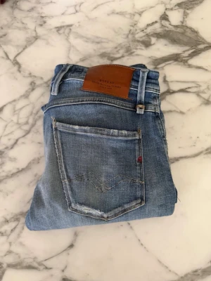 Ljusblå jeans från Replay - Snygga ljusblå jeans från Replay med slitna detaljer och klassisk femficksdesign. Jeansen har en skön passform och är tillverkade i denim med en lätt tvättad look. Perfekta för en avslappnad stil.