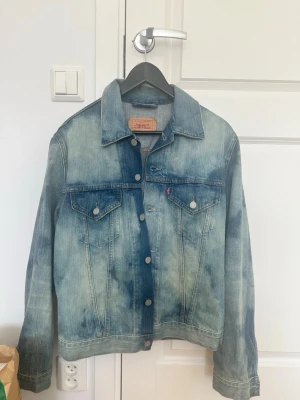 Vintage Levi's jeansjacka - Klassisk jeansjacka från Levi's i mellanblå tvättad denim med ljusa partier. Jackan har två bröstfickor med knappar, knappstängning framtill och en avslappnad passform. Perfekt för en cool och tidlös stil.