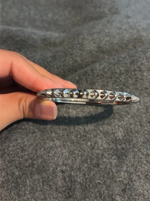 Silvrigt armband med nitar Edblad  - Snyggt armband i silverfärg med coola pyramidformade nitar runt hela. Armbandet är stelt och har en modern, edgy vibe som verkligen sticker ut. Perfekt accessoar för att lyfta din outfit med lite extra attityd.