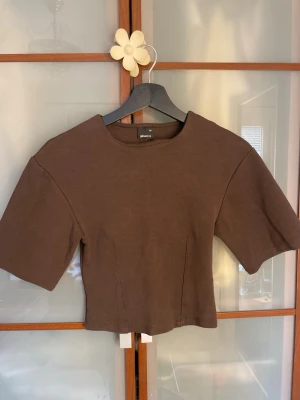 Brun topp från Gina Tricot - Snygg brun topp från Gina Tricot i storlek XS. Modellen har korta ärmar och en rund halsringning. Materialet känns mjukt och stretchigt, perfekt till jeans eller kjol. Enkel och stilren design som är lätt att matcha.