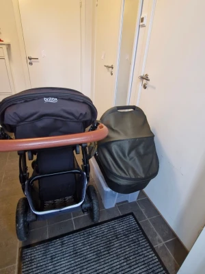 Svart barnvagn Britax Smile - Säljer enbarnvagn Britax Smile med robust ram i metall och detaljer i brunt konstläder på handtaget. Vagnen har stora hjul, rymlig varukorg undertill och justerbart ryggstöd. Perfekt för promenader och enkel att manövrera.