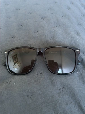 Bruna Wayfarer solglasögon Ray-Ban - Klassiska svarta Wayfarer solglasögon från Ray-Ban med bred båge och mörka glas. Snygg och tidlös design med Ray-Ban-logga på båda sidor. Perfekta för att lyfta vilken outfit som helst.