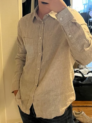 Snygg och fräsch j.lindeberg linneskjorta - Säljer en stilren beige skjorta i linne med lång ärm och klassisk krage. Skjortan har knappar framtill och en bröstficka. Perfekt för en avslappnad men ändå snygg look.