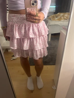 Rosa volangkjol med blommigt mönster - Säljer en jättefin kort kjol med volanger och rosa blommor, säljer för att den inte kommer till användning❣️❣️