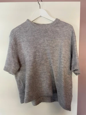 Ljusgrå stickad tröja Gina Tricot - Mysig ljusgrå stickad tröja från Gina Tricot med korta ärmar och rund hals. Tröjan har ribbade kanter vid hals, ärmslut och nederkant. Tillverkad i ett mjukt material som känns lyxigt och passar perfekt för lager på lager.