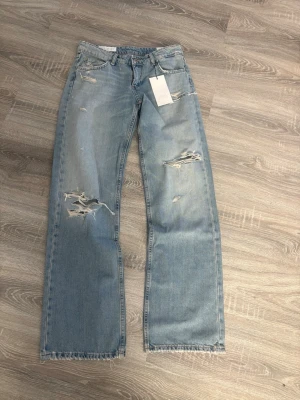 Ljusblå slitna raka jeans - Säljer ett par ljusblå jeans från Zara med raka ben och slitningar på både fram- och baksida. Jeansen har fransiga benslut och klassisk femficksmodell. Perfekta för en avslappnad och trendig look.