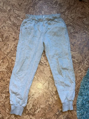 Ljusgrå mjukisbyxor med resår i midjan - Säljer ett par ljusgrå mjukisbyxor i storlek S,  med resår i midjan och breda muddar vid bensluten. Tror dom är från H&M och har en avslappnad passform i mjukt bomullsmaterial. Byxorna har en liten orange fläck på framsidan ca 1cm nedåt från resåren, annars inga defekter. Säljes pga för små🤩☺️