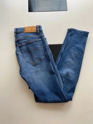 Blå slim fit jeans i modell Evolve - Snygga blå slim fit jeans i modellen Evolve med klassisk femficksdesign och kontrastsömmar. Jeansen har en skinnpatch i midjan och är tillverkade i ett mjukt denimtyg som ger en bekväm passform. Perfekta för en avslappnad och trendig look.