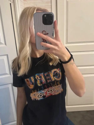 Svart t-shirt med färgglatt tryck - Cool svart t-shirt med stort färgglatt tryck på bröstet där det står 'CEBU' och ett mönster inspirerat av filippinsk design. T-shirten har rund hals och korta ärmar. Perfekt för dig som gillar unika prints och streetstyle.