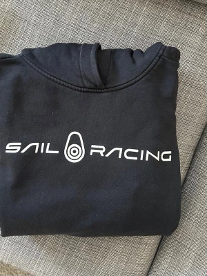 Svart hoodie från Sail Racing. Storlek 170. Ungdom - Säljer en svart hoodie från Sail Racing med vit logga och text på bröstet. Storlek 170. Ungdom
