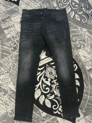 Svarta Dsquared2 Jeans - Snygga svarta slim fit jeans med slitningar och lätt tvättade detaljer på benen. Jeansen har fem fickor, dubbla knappar i midjan och smal passform. Perfekta för en trendig och avslappnad stil.