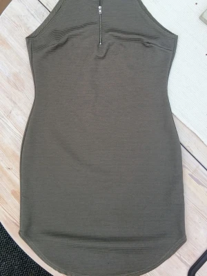 kort klänning från Boohoo - Snygg olivgrön kort klänning från Boohoo med hög hals och dragkedja framtill. Klänningen är ärmlös och har en tight passform med ribbad struktur. Perfekt för dig som gillar en stilren och modern look. Passar såväl till vardags som till fest