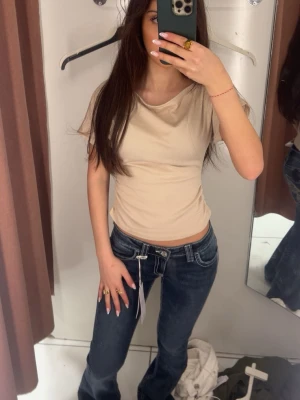 Mörkblå bootcut jeans med broderi - Säljer ett par mörkblå bootcut jeans med snygga kontrastsömmar och broderade bakfickor. Jeansen har låg midja och klassisk femficksdesign. Perfekta för dig som gillar en avslappnad men trendig look.