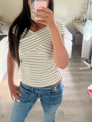 Randig omlottopp från Zara - Säljer en snygg vit omlottopp från Zara med svarta horisontella ränder. Toppen har en unik omlottdesign över axlarna och är ärmlös. Säljer för att jag köpte en för liten storlek och tog redan bort lappen innan. Köpte tröjan för 219kr.