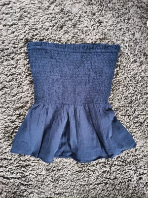 Mörkblå smockad linnetopp - Snygg mörkblå linnetopp med smockad överdel och volang nedtill från Gina Tricot. Toppen har tunna axelband som går att ta av för en axelbandslös look. Perfekt för sommarens alla outfits och ger en feminin siluett. 