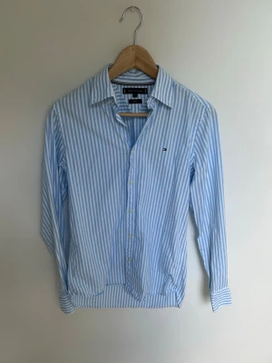 Blåvit randig skjorta Tommy Hilfiger - Klassisk blåvit randig skjorta från Tommy Hilfiger med lång ärm och knappar framtill. Skjortan har en liten logga på bröstet och är tillverkad i bomull. Perfekt för en stilren och fräsch look.