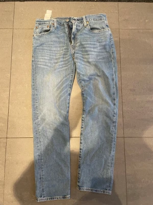 Levi's jeans 502 - Säljer ett par klassiska ljusblå Levi's jeans med rak passform och fem fickor. Jeansen har en vintage vibe med den ikoniska läderlappen bak i midjan och röda Levi's-taggen på bakfickan. Tillverkade i slitstark denim, perfekta för en avslappnad look.