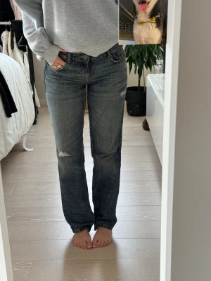 Mörkblå raka jeans med slitningar - Säljer ett par mörkblå jeans med raka ben och snygga slitningar på låren och knäna. Jeansen har klassisk femficksdesign och låg midja. Perfekta för en avslappnad och trendig look.