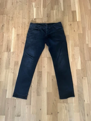 Svarta slim fit jeans från Jack & Jones - Säljer ett par svarta slim fit jeans från Jack & Jones. Jeansen har klassisk femficksdesign, smal passform och är tillverkade i stretchigt denimtyg för extra komfort. Perfekta för en trendig och avslappnad stil.
