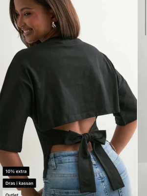 Svart croppad topp med knyt i ryggen - Trendig svart croppad topp med halvlånga ärmar och snygg öppen rygg som knyts med en stor rosett. Perfekt för dig som vill ha en unik twist på din outfit. Tillverkad i mjukt bomullstyg för skön känsla.