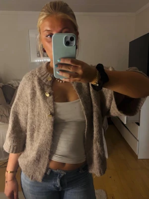 Beige kofta neo noir - Mysig beige kofta med korta ärmar och rund hals. Koftan har tre dekorativa guldknappar framtill och är stickad i ett fluffigt material. Köpte den förra året och andvänd en gång, den är jätteskönt och köpt från neo noir. Skriv privat för fler frågor!❤️ nypris 899!