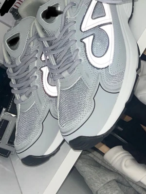 CD B30  - (Box ingår )Snygga sneakers i ljusgrått med reflekterande vita detaljer på sidorna. Ovandelen är i mesh och syntetmaterial för bra andningsförmåga. Tjock vit sula och grå skosnören ger en modern look. Perfekta för dig som gillar stilrena och sportiga skor.