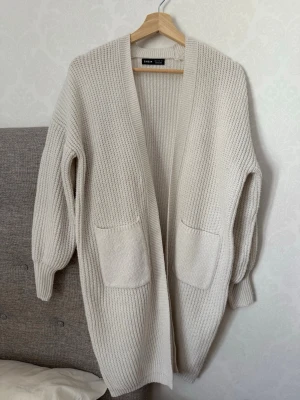 Beige stickad kofta från SHEIN - Mysig beige stickad kofta från SHEIN med öppen front och två stora fickor framtill. Koftan har en avslappnad passform och ribbstickad struktur, perfekt att slänga över en t-shirt eller topp. Långa ärmar och mjukt material.
