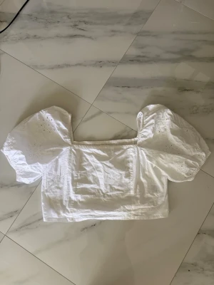 Vit blus med puffärmar och broderi - Supersöt vit blus med fyrkantig ringning och stora puffärmar. Ärmarna har broderade hål och ger en romantisk vibe. Toppen är croppad och gjord i bomull. Storlek L men passar mer S/M då den är liten i storleken. 