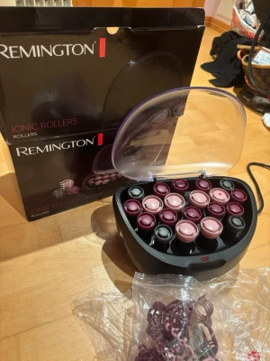 Remington värmespolar i vinrött och rosa - Säljer ett set med Remington värmespolar i olika storlekar, perfekta för att skapa volym och lockar. Spolarna är i vinrött och ljusrosa och kommer med tillhörande clips. Förvaringsbox med genomskinligt lock och sladd för uppvärmning ingår.