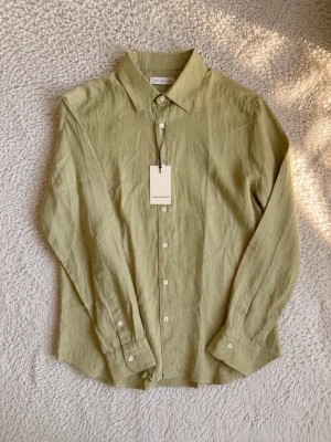 these glory days beige/olivgrön linneskjorta – ny med lapp - Riktigt stilren skjorta från These Glory Days i en snygg beige/olivgrön ton. Den tunna och luftiga känslan gör den perfekt för vår och sommar, och färgen fungerar otroligt bra tillsammans med både vitt, beige, svart och denim.  En minimalistisk modell som enkelt kan kläs upp eller ner. Helt ny och aldrig använd med originalprislappen kvar.