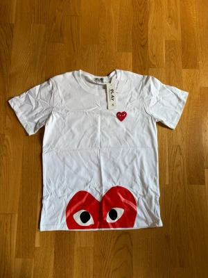 Vit t-shirt Comme des Garçons Play - Säljer denna fina T-shirt . ✨  📌 Storlek: [S] 📌 Skick: [mycket bra/oanvänd] 📌 Färg: [vit/röd] 📌 Passform: [slim fit]  📦 Skickas snabbt och välpackat!