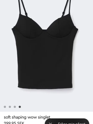 Svart shaping singlet topp med smala band - Snygg svart shaping singlet topp med tunna axelband och markerade kupor. Toppen har en croppad passform och ger en smickrande siluett. Perfekt att styla till jeans eller kjol för en trendig look. Toppen är helt ny och aldrig använd, prislappen sitter kvar 