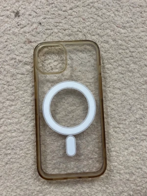 Transparent MagSafe mobilskal brun kant - Snyggt transparent mobilskal med bruna kanter och inbyggd MagSafe-ring i vitt. Skalets material är tålig plast och det har en öppning för kamera i hörnet. Passar perfekt för dig som vill visa upp din mobil men ändå skydda den. iPhone 13,14,15