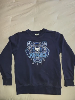 Mörkblå Kenzo sweatshirt med tiger - Cool mörkblå sweatshirt från Kenzo med ikoniskt tigerbroderi och texten 'Kenzo Paris' framtill. Tröjan har rund hals, ribbade muddar och är perfekt för dig som gillar streetstyle och snygga detaljer.