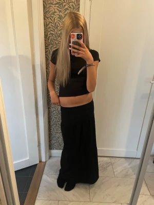Svart långkjol med enkel design - En svart långkjol med rak passform och minimalistisk look. Kjolen har en hög midja och faller snyggt längs benen. Perfekt att matcha med crop tops eller stickade tröjor för en trendig stil.