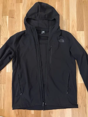 North Face windbreaker - Snygg svart vindjacka från The North Face med huva och dragkedja framtill. Jackan har tre fickor med dragkedja och diskret logga på bröstet. Tillverkad i ett lätt och tåligt material som passar perfekt för blåsiga dagar. Storlek M. Perfekt skick utan defekter. Pris kan diskuteras