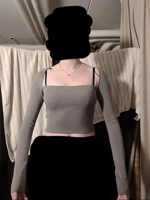 Grå ribbad croppad topp - Trendig grå croppad topp med långa ärmar och ribbad struktur. Toppen är figurnära och har en stilren, minimalistisk look som passar perfekt till jeans eller kjol. Axelbandslös design med raka linjer för en modern vibe.